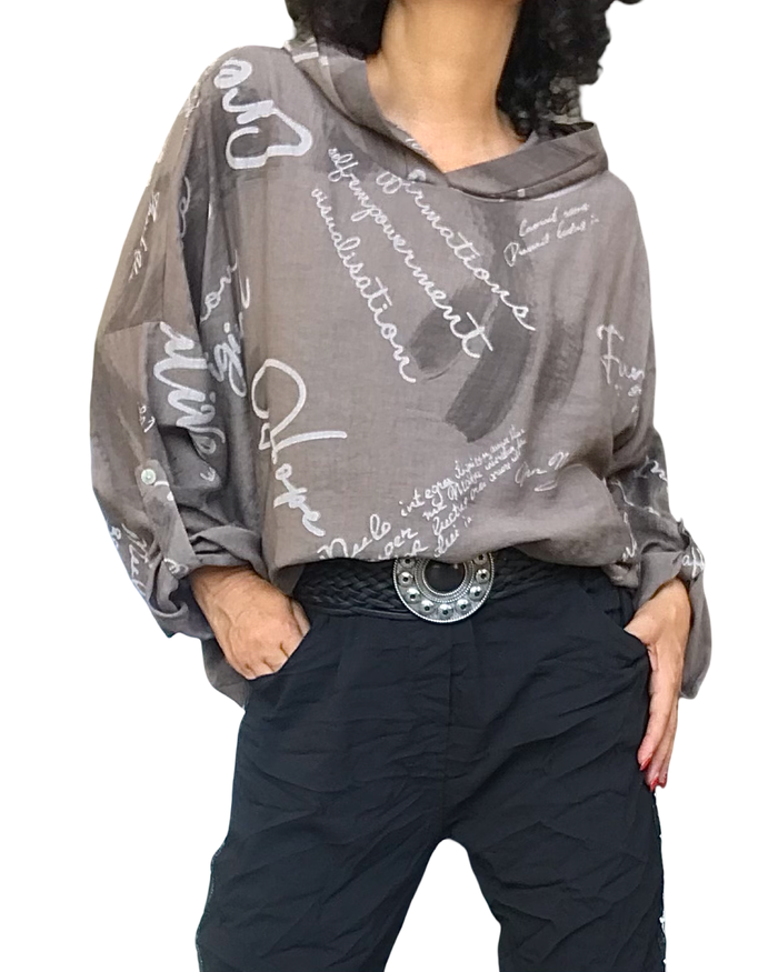 Tunique brune à écritures beige et capuchon portée avec ceinture à boucle argentée et pantalon noir