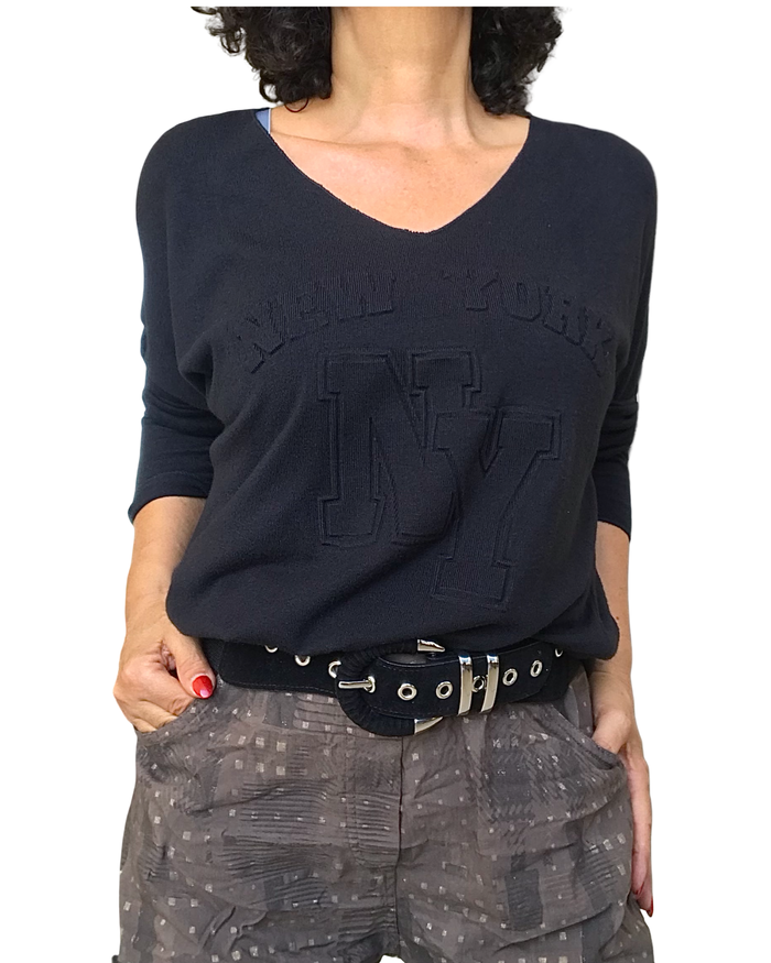 Chandail noir col V avec « New York » embossé, porté avec ceinture noire et pantalon gris imprimé